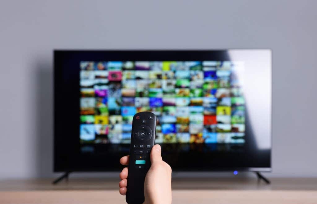 Hand holding a remote control pointed at a smart TV displaying a grid of streaming app thumbnails